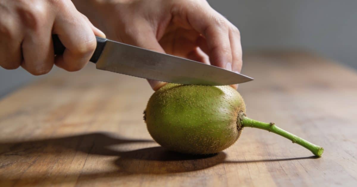 Mains coupant une tige de kiwi sur table