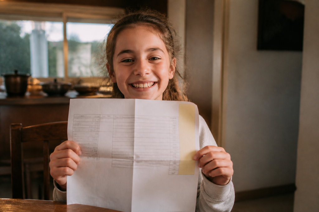 Enfant souriant tenant un bulletin scolaire aux bonnes notes