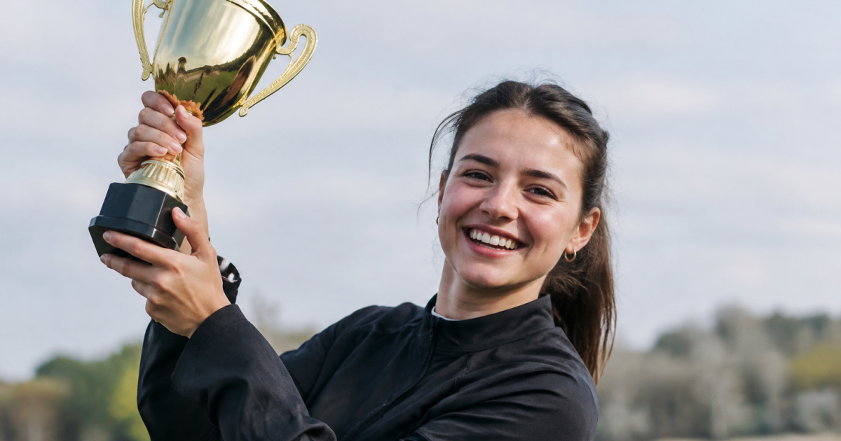 Jeune femme souriante levant un trophee dore
